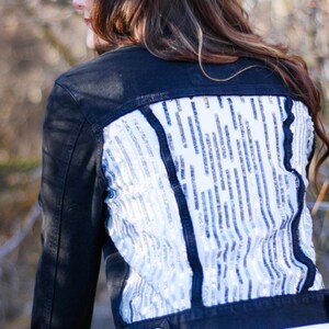 May include: A black denim jacket with a white sequined back panel. The sequins are arranged in a wavy pattern.