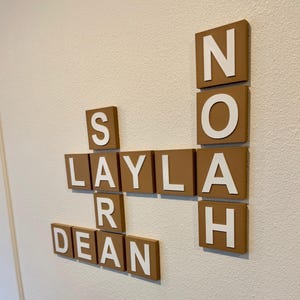 May include: Wooden wall decor spelling out the names Layla, Dean, and Noah. The letters are white against a brown background. The decor is mounted on a textured, off-white wall.
