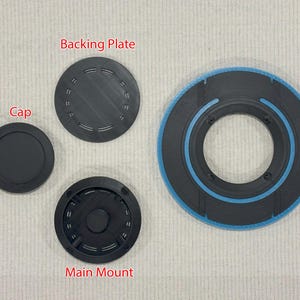 May include: An assortment of black, circular components. The image includes a cap, a backing plate, and a main mount, all in black. A larger, circular piece with a blue accent is also present. The components appear to be 3D-printed.