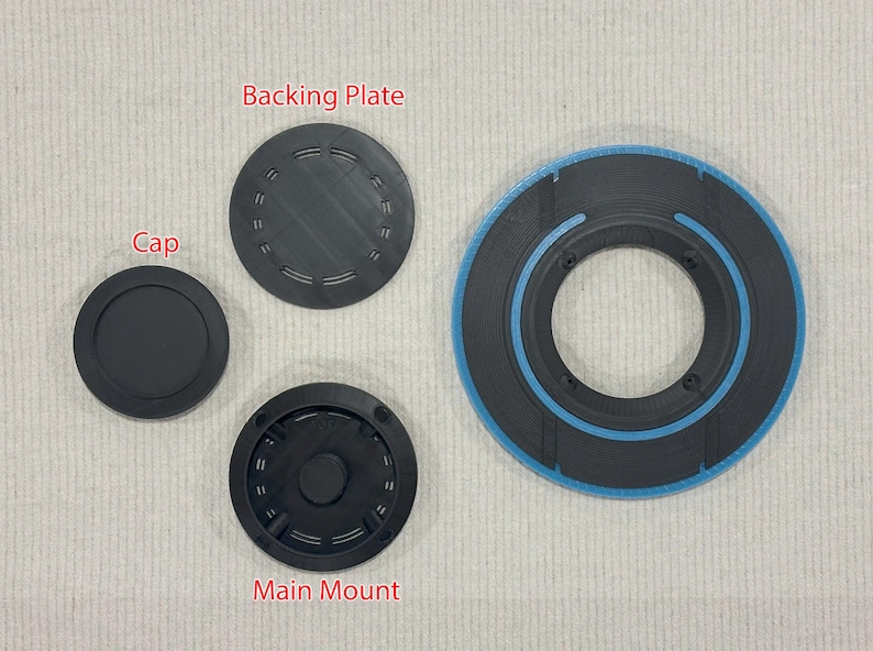 May include: An assortment of black, circular components. The image includes a cap, a backing plate, and a main mount, all in black. A larger, circular piece with a blue accent is also present. The components appear to be 3D-printed.