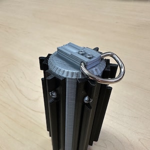 Puede incluir: Un sable de luz impreso en 3D de color negro y plateado con un mango plateado y un mango de anillo negro. El sable de luz tiene una parte superior plateada con un anillo negro.