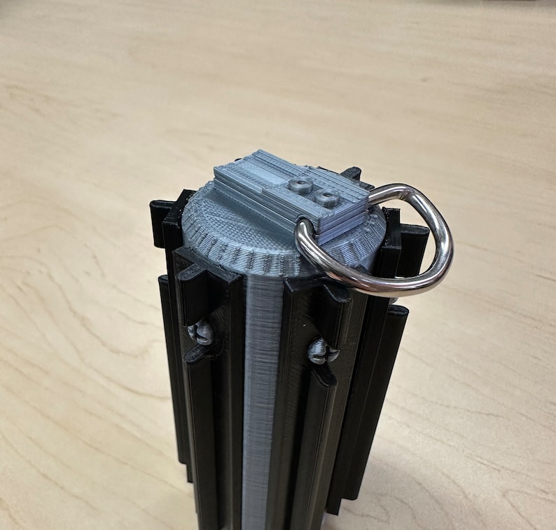 Puede incluir: Un sable de luz impreso en 3D de color negro y plateado con un mango plateado y un mango de anillo negro. El sable de luz tiene una parte superior plateada con un anillo negro.