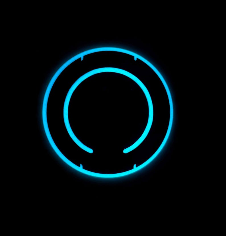 May include: A glowing, neon-blue circular design against a black background. The design features two concentric circles, with small breaks in the outer ring. The bright blue color creates a striking contrast against the dark backdrop.