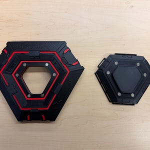 May include: Two black and red geometric objects with a hexagonal shape. The larger object has a central opening and red accents. The smaller object is solid black. Both have metallic accents.