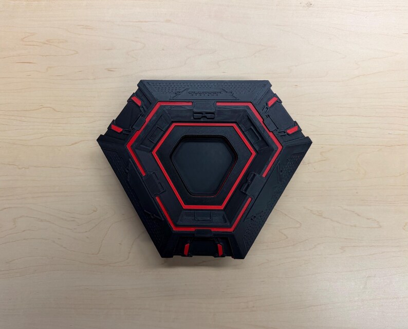 May include: A black and red hexagonal object with a recessed center. The object has a geometric design with red accents and a textured surface. The overall design is modern and industrial.