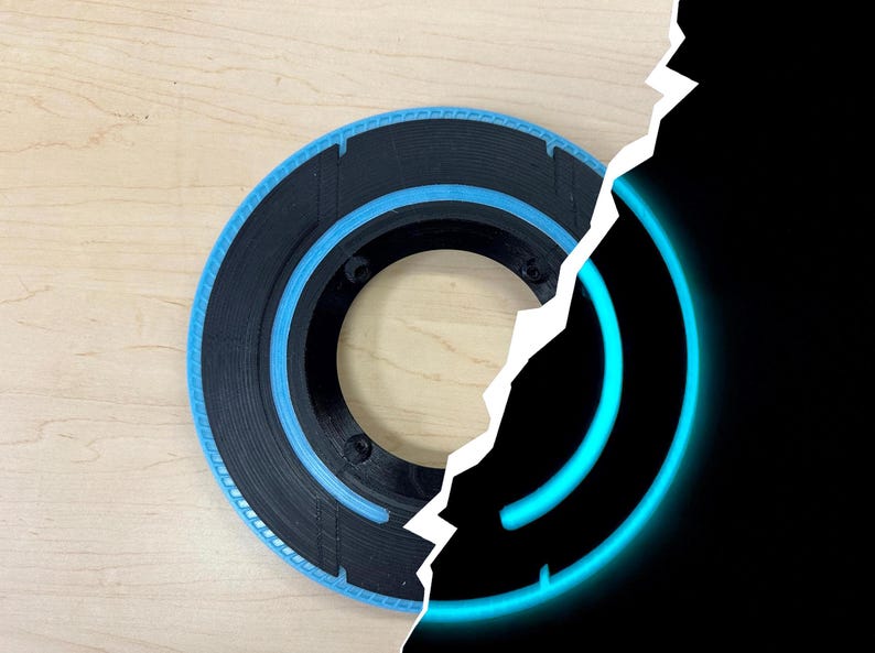May include: A black and blue circular object with a central hole, possibly a speaker component or decorative element. The object has a blue ring and a black outer ring. The background is a light wood surface.