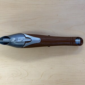 May include: A brown and silver object with a pointed end and a cylindrical base. The object has a metallic silver tip and accents, with a textured brown handle. The design includes a series of silver bolts and a circular opening at the base.