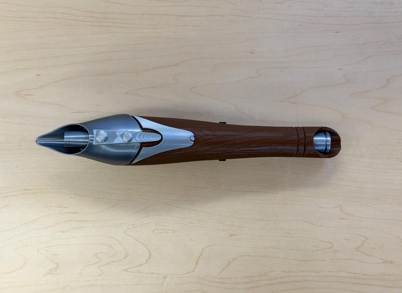 May include: A brown and silver object with a pointed end and a cylindrical base. The object has a metallic silver tip and accents, with a textured brown handle. The design includes a series of silver bolts and a circular opening at the base.