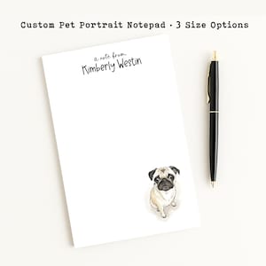May include: A white rectangular notepad featuring the printed text a note from Kimberly Westin at the top and a watercolor illustration of a tan and black pug dog at the bottom right corner, accompanied by a black ballpoint pen with gold accents.