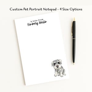 May include: A white rectangular notepad featuring a watercolor illustration of a gray and white schnauzer puppy in the bottom right corner. The text at the top reads a note from Kimberly Westin. A black ballpoint pen is positioned to the right.