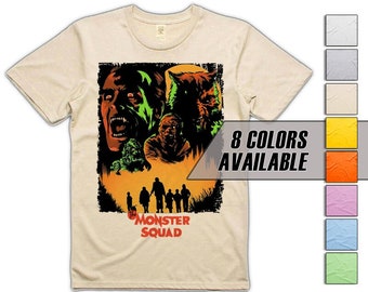May include: A beige t-shirt featuring a graphic print of the film "The Monster Squad". The graphic depicts a werewolf, a vampire, a mummy, and a Frankenstein's monster. The text "The Monster Squad" is printed beneath the graphic. 8 colours are available.