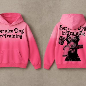 May include: A pink hoodie with the text "Service Dog in Training" on the front. The back features a black and white graphic of a dog holding a gun, with the text "I said don't fuckin' pet me!"