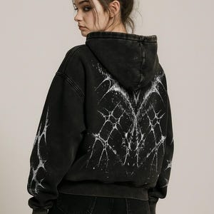 Puede incluir: Sudadera con capucha negra con un diseño gráfico blanco desgastado en la espalda y las mangas. La sudadera tiene una capucha con cordón y puños acanalados. La marca "CROWCO" está impresa en fuente gótica en la parte inferior derecha.