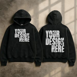 Puede incluir: Sudadera con capucha negra con el texto "YOUR DESIGN HERE" en letras blancas desgastadas en la parte delantera y trasera. La sudadera tiene capucha y bolsillo delantero. La tela tiene un aspecto vintage.