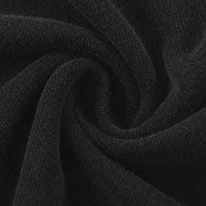 Op de afbeelding: Close-up van zwarte stof met zichtbare textuur en vouwen. Het materiaal lijkt een strak geweven breisel te zijn, met een licht matte afwerking. De donkere kleur en textuur suggereren een kledingstuk of textiel.