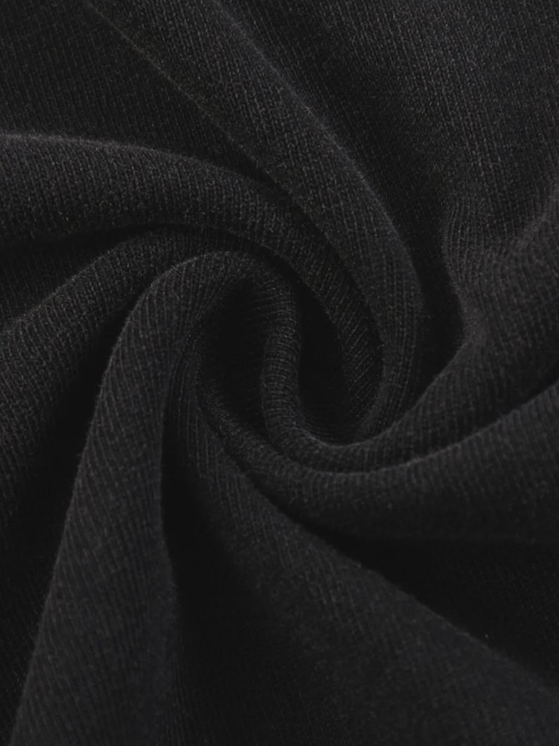 Op de afbeelding: Close-up van zwarte stof met zichtbare textuur en vouwen. Het materiaal lijkt een strak geweven breisel te zijn, met een licht matte afwerking. De donkere kleur en textuur suggereren een kledingstuk of textiel.