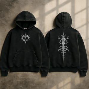 Op de afbeelding: Zwarte hoodie met een voorzak en capuchon. De voorkant heeft een zilverkleurig hartvormig ontwerp, terwijl de achterkant een ruggengraatachtige afbeelding toont. De hoodie is gemaakt van een zacht, comfortabel materiaal.