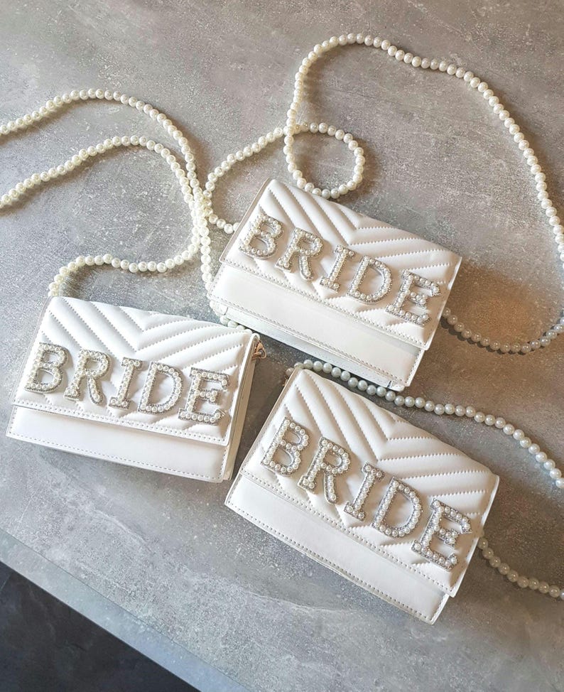 May include: Three white quilted purses with pearl straps. Each purse has the word "BRIDE" spelled out in rhinestones.