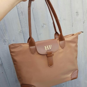 May include: A brown tote bag with a leather strap and buckle closure. The bag has a monogrammed patch with the initials "HF" in gold lettering.