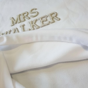 May include: White sweatshirt with the text "MRS WALKER" in pearl-like embellishments. The sweatshirt has a soft, fleecy interior and a ribbed neckline. The design is centered on the upper chest.
