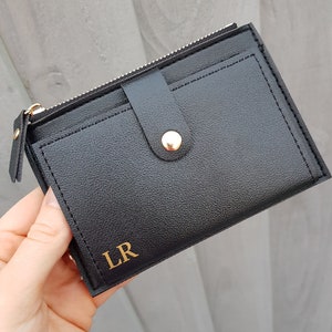 May include: A black leather wallet with a gold zipper and a gold button closure. The wallet has a flap with a gold snap closure and the initials "LR" are embossed on the front.