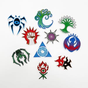 Puede incluir: Colección de parches bordados con varios símbolos de fantasía. Los parches incluyen una araña azul con un ojo, un árbol verde, un puño rojo, una estrella púrpura y otros diseños coloridos. Estos parches son probablemente para ropa o accesorios.