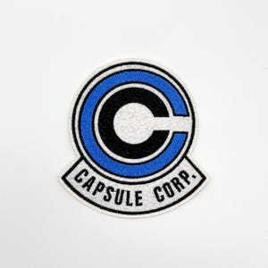 May include: Embroidered patch featuring the Capsule Corp. logo from Dragon Ball. The patch has a white background with a blue and black circular design and the text "CAPSULE CORP."