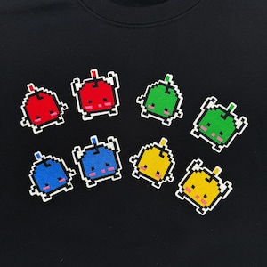 May include: Black sweatshirt featuring a pattern of pixelated, colorful alien-like creatures. The creatures are in red, green, blue, and yellow with white outlines and pink accents. The design is repeated across the front of the shirt.