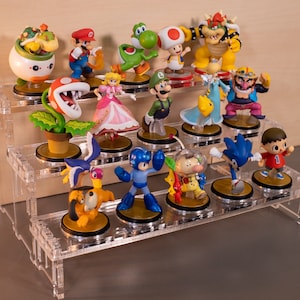 May include: A three-tiered acrylic display stand with 18 colourful figurines of popular video game characters, including Mario, Luigi, Peach, Bowser, Yoshi, and Sonic the Hedgehog.