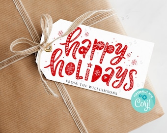 May include: A white rectangular gift tag with a gold eyelet and natural twine, featuring the red text "happy holidays" in a stylized script font with snowflake accents and the text "FROM, THE WILLIAMSONS" printed in black.