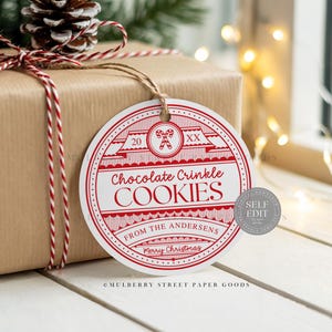 May include: A wrapped gift with a red and white twine bow and a round gift tag. The tag reads "Chocolate Crinkle Cookies" with "From The Andersens" and "Merry Christmas" in red text.