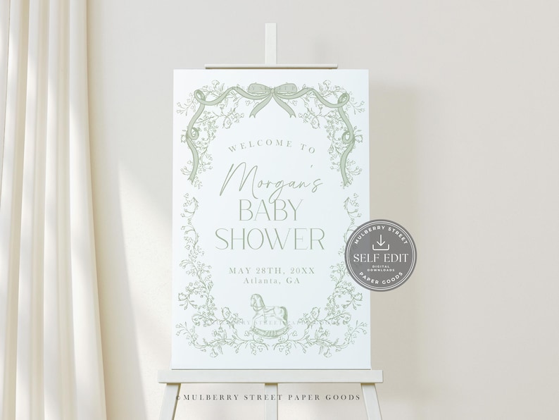 Pu&ograve; includere: Un cartello bianco per baby shower su un cavalletto, con un design floreale verde e la scritta "Benvenuti al baby shower di Morgan". Il cartello include la data e il luogo. Un adesivo "Self Edit" &egrave; a destra.