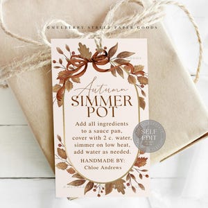 May include: A gift tag with the text "Autumn Simmer Pot" in an oval frame, decorated with brown leaves and a bow. The tag includes instructions and is tied to a wrapped package with twine.