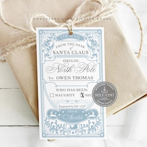 Puede incluir: Una etiqueta de regalo con un diseño azul claro y blanco, atada a un paquete envuelto con hilo. La etiqueta dice "From the Desk of Santa Claus, Origin: North Pole, To: Owen Thomas". La etiqueta también tiene una sección para marcar si el destinatario ha sido travieso o bueno.