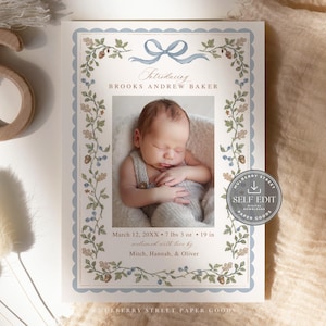 May include: A birth announcement card featuring a central photograph of a newborn baby. The card has a light blue scalloped border, a blue ribbon graphic, and botanical illustrations of leaves, acorns, and berries. Text includes the name Brooks Andrew Baker, birth details, and the names Mitch, Hannah, and Oliver.