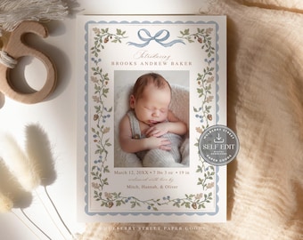 May include: A birth announcement card featuring a central photograph of a newborn baby. The card has a light blue scalloped border, a blue ribbon graphic, and botanical illustrations of leaves, acorns, and berries. Text includes the name Brooks Andrew Baker, birth details, and the names Mitch, Hannah, and Oliver.