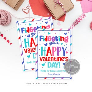 May include: Two Valentine's Day cards with the text "Fidgeting you a HAPPY Valentine's DAY!" in colourful letters. The cards are decorated with hearts and surrounded by gift boxes, washi tape, and other Valentine's Day themed items.
