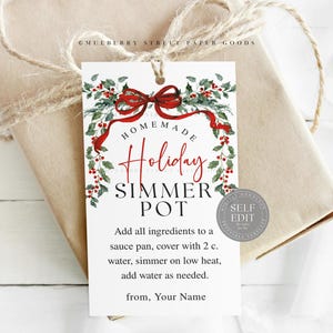 May include: A white gift tag with the text "HOMEMADE Holiday SIMMER POT" in red and black, surrounded by a festive wreath with red berries and a red bow. The tag is tied to a wrapped gift with twine.