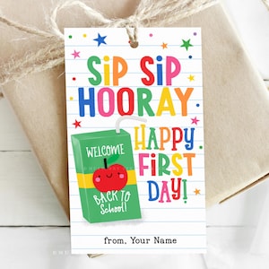 May include: A gift tag with the words "SIP SIP HOORAY HAPPY FIRST DAY!" in colorful letters. A green juice box with a smiling red apple and the words "WELCOME BACK TO SCHOOL!" is featured. The tag is tied to a wrapped gift.