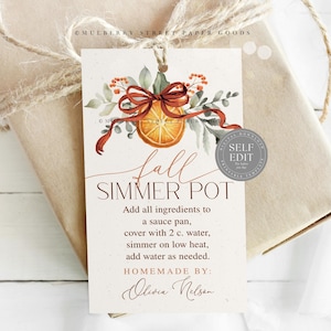 May include: A gift tag with a watercolor design for a fall simmer pot. The tag features an orange slice, leaves, and a ribbon. Text on the tag reads "Fall Simmer Pot" and instructions. The tag is tied to a wrapped gift with twine.