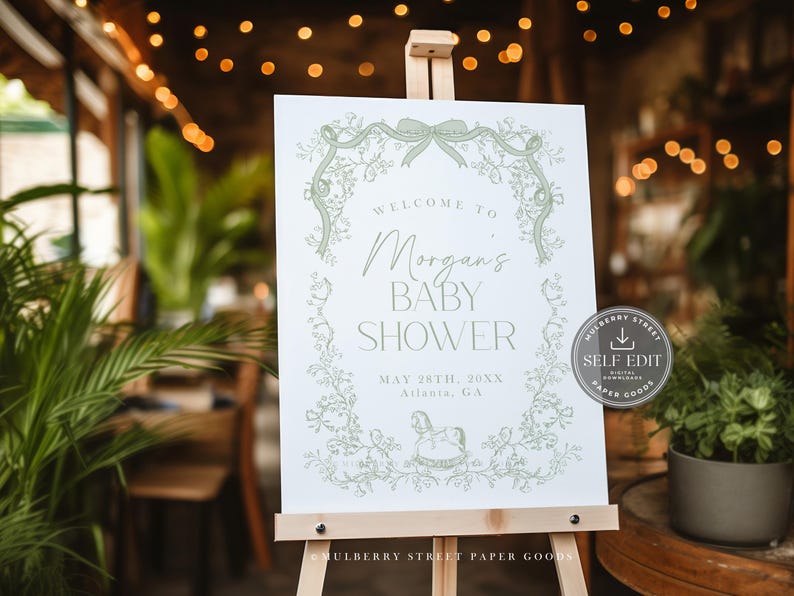 Pu&ograve; includere: Un cartello bianco su un cavalletto con la scritta "Benvenuti al Baby Shower di Morgan" in verde. Il cartello include la data e il luogo ed &egrave; decorato con illustrazioni floreali e fiocchi. Un adesivo con "Self Edit" &egrave; a destra.