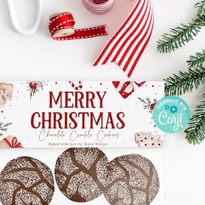 以下が含まれることがあります： 赤と白のストライプのリボンが付いた白いギフトボックス。ボックスには、「メリークリスマス チョコレートクランブルクッキー」と「Katie Wilsonより愛を込めて」と書かれたラベルが付いています。ボックスは緑の松の枝と赤と白のストライプのリボンで囲まれています。