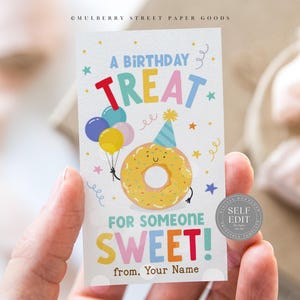 May include: A birthday treat gift tag with a cartoon donut holding balloons. The card has the text "A BIRTHDAY TREAT FOR SOMEONE SWEET!" in colorful letters. The tag is held in a person's hand.