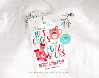 May include: A white gift tag with a red and green illustration of a mug of hot chocolate, fuzzy socks, and the text "Here's to hot chocs and fuzzy socks Merry Christmas from, Madison".