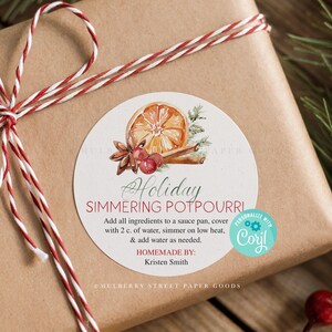 May include: A wrapped gift with a round label that reads "Holiday Simmering Potpourri." The label features a watercolor illustration of an orange slice, cinnamon sticks, and berries. The gift is wrapped in brown paper and tied with red and white twine.