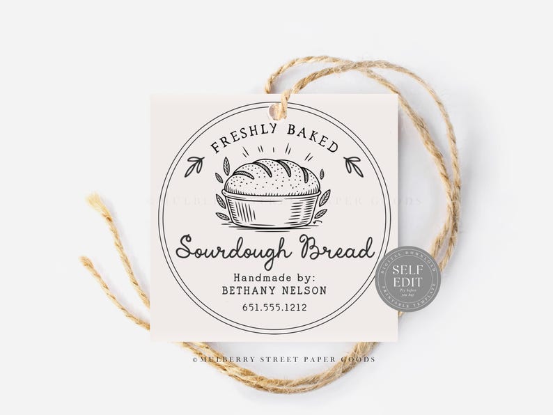 Puede incluir: Una etiqueta cuadrada de color blanquecino con un dise&ntilde;o circular que presenta un pan de masa madre. El texto dice "FRESHLY BAKED Sourdough Bread" y "Handmade by: BETHANY NELSON 651.555.1212". La etiqueta est&aacute; atada con hilo natural.