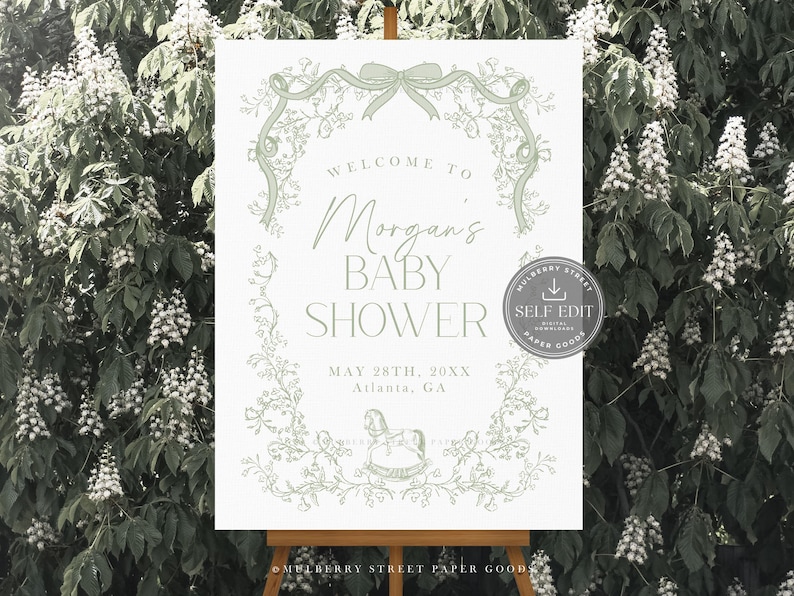 Pu&ograve; includere: Un cartello per baby shower su un cavalletto, con la scritta "Welcome to Morgan's Baby Shower" in un elegante carattere. Il design include elementi floreali e un'illustrazione di un cavallo a dondolo, con la data e il luogo sottostanti.