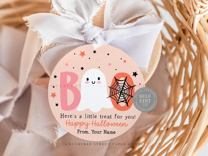 May include: A round Halloween gift tag with a light pink background. The tag features a ghost, spiderweb, and the word "BOO" in pink. Text reads "Here's a little treat for you! Happy Halloween From, Your Name."