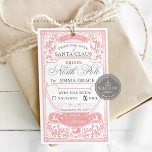 Puede incluir: Una etiqueta de regalo rosa y blanca atada a un paquete envuelto con hilo. La etiqueta dice "From the Desk of Santa Claus" e incluye espacio para el nombre del destinatario y una casilla de verificación para "Naughty" o "Nice".