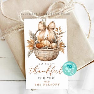Puede incluir: Una etiqueta de regalo blanca con una ilustración de acuarela de una cesta llena de calabazas y hojas de otoño. El texto dice "So very thankful for you! from, THE NELSONS".